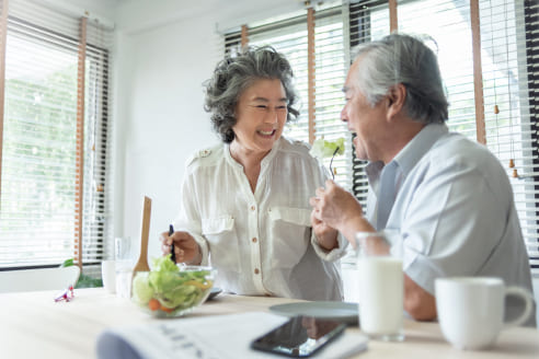 微笑みあいながらサラダを食べている老夫婦